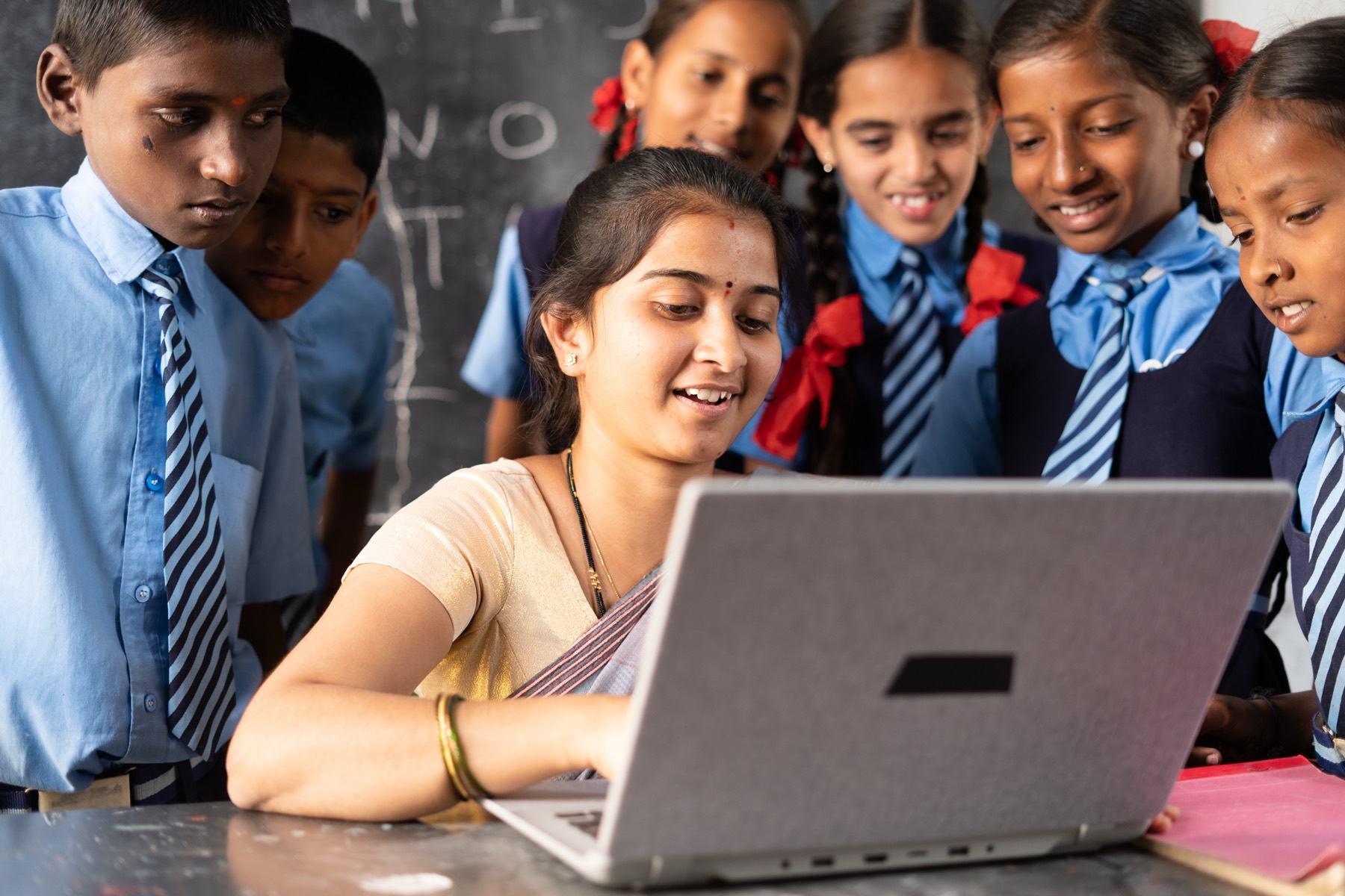 A teacher showing a laptop to smiling school students